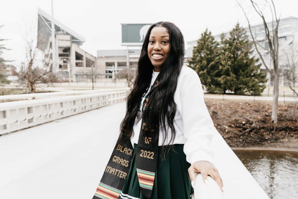 Re'Anna, a Black woman with long black hair smiling in front of Spartan Stadium.