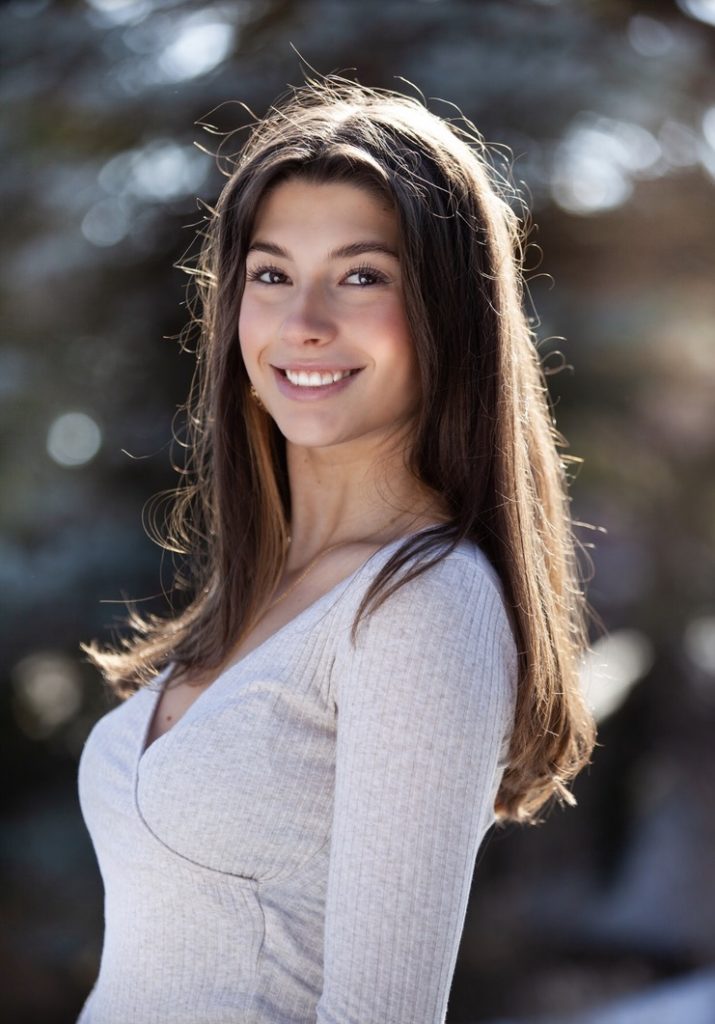 A white-presenting woman with long dark hair and a white top smiling