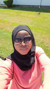 A woman of color wearing a hijab, sunglasses, and a pink top