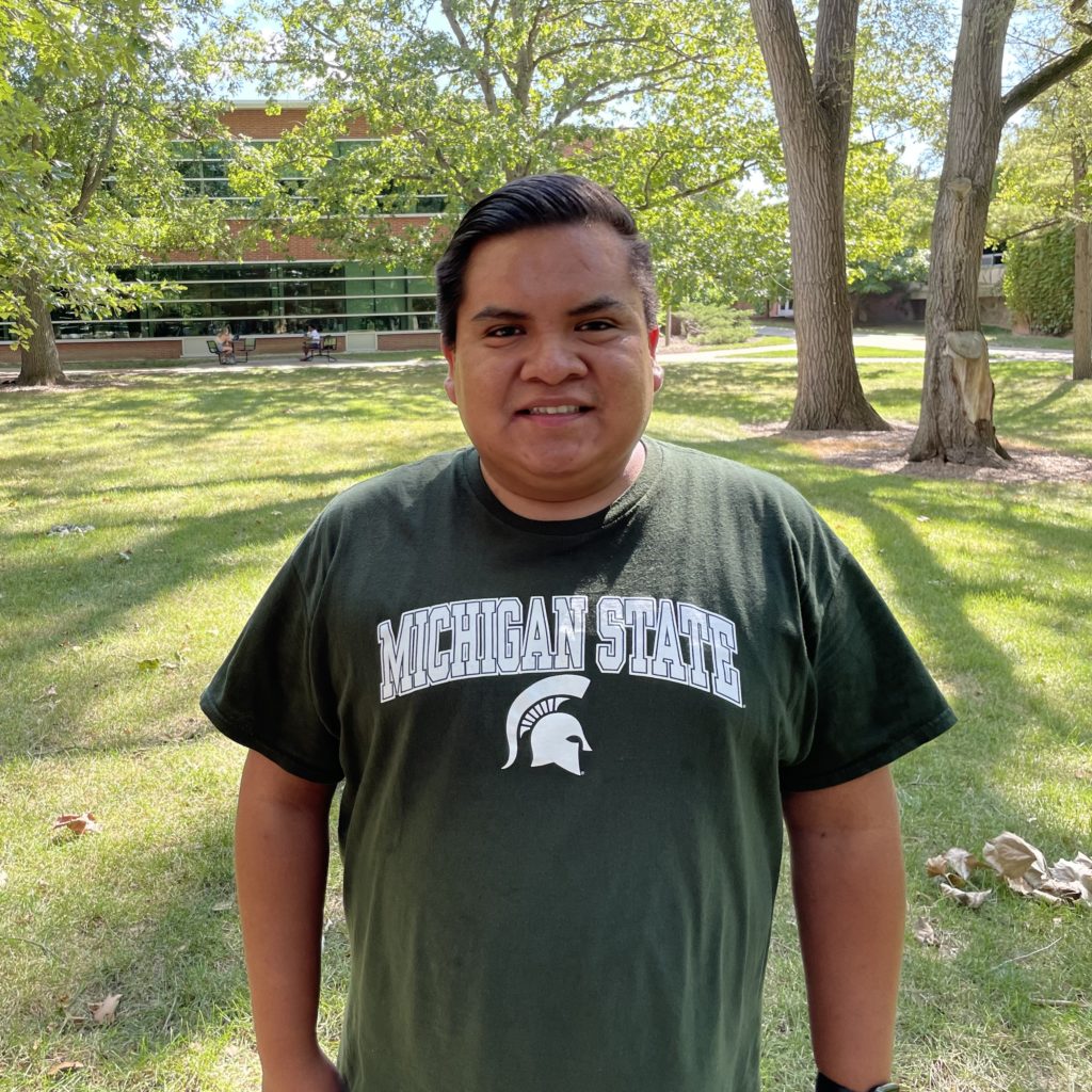 Orville, a male with short dark brown hair. With a Michigan State t-shirt in a outdoor setting.