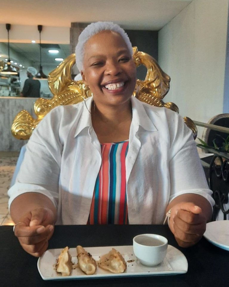 Tshepang, an African woman with white bleached short hair, sitting at a restaurant table smiling