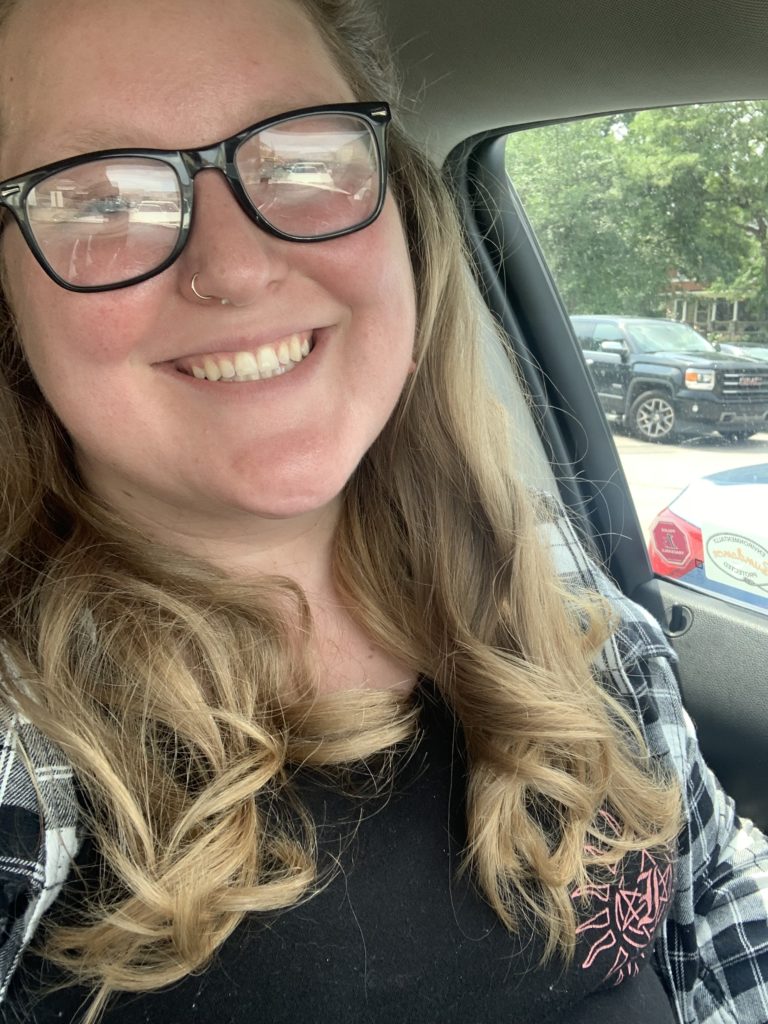 Annabelle, a white woman with long blond hair and black-rimmed glasses, smiling in a car.